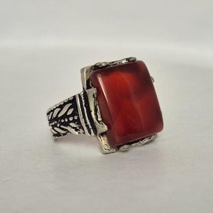 Peut inclure: Une bague en argent avec un motif orné et une grande pierre rouge rectangulaire.