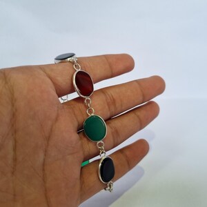 May include: A silver bracelet with four oval-shaped stones. The stones are black, red, green, and black.