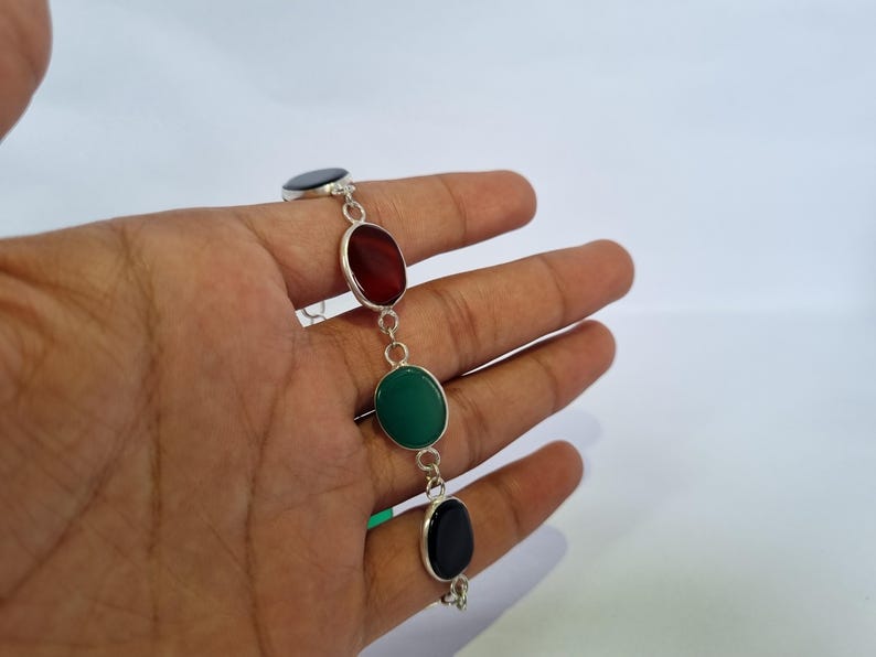 May include: A silver bracelet with four oval-shaped stones. The stones are black, red, green, and black.