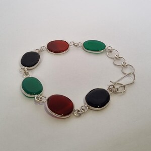 May include: A silver bracelet with alternating black, red, and green oval stones.