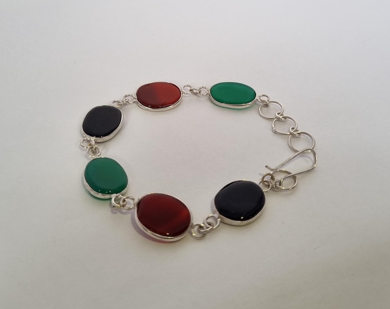 May include: A silver bracelet with alternating black, red, and green oval stones.