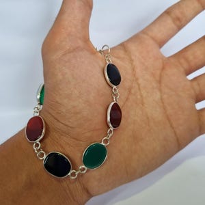 May include: A silver bracelet with oval-shaped gemstones in shades of green, red, and black.