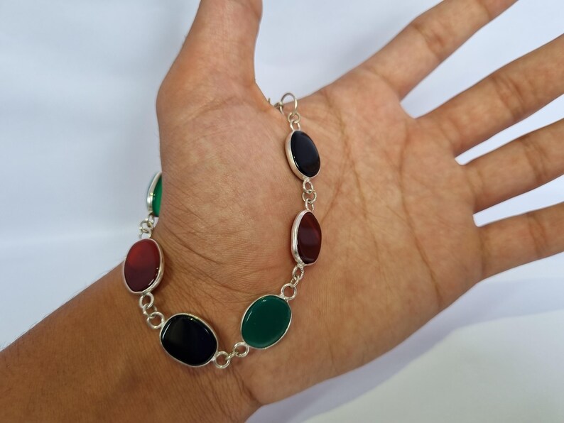 May include: A silver bracelet with oval-shaped gemstones in shades of green, red, and black.
