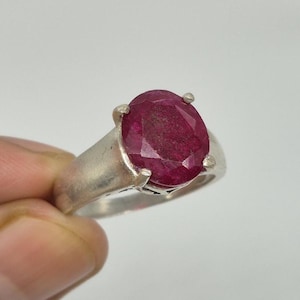Könnte beinhalten: Ein silberner Ring mit einem großen, oval geschliffenen Rubin. Der Rubin hat eine tiefe, satte rote Farbe und wird von vier Krappen gehalten. Der Ring hat ein schlichtes, klassisches Design.