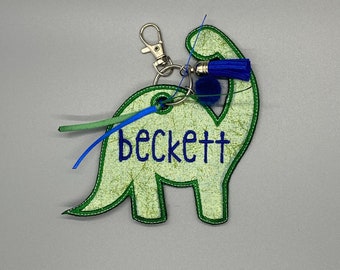 May include: Green dinosaur-shaped keychain with a blue tassel and the name "beckett" embroidered in blue thread.