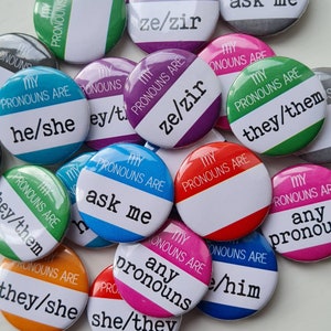 Könnte beinhalten: Eine Sammlung bunter Pronomen-Ansteckbuttons mit Texten wie "he/she", "they/them" und "ask me". Die Buttons sind rund mit weißem Text auf farbigem Hintergrund, und der Satz "MY PRONOUNS ARE" ist ebenfalls auf jedem Button aufgedruckt.