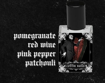 May include: A small bottle of perfume with a black cap and a label that says "coffin nails". The label features a black and white illustration of a man in a suit holding a red coffin. The text on the label also lists the fragrance notes: pomegranate, red wine, pink pepper, and patchouli.