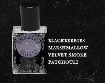 May include: A small glass bottle of perfume with a black cap and a label that says "Strange Magic". The label is surrounded by a decorative border. The text "Blackberries, Marshmallow, Velvet Smoke, Patchouli" is printed below the bottle.