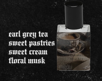 May include: A clear glass bottle of perfume with a black cap. The label reads "sweater weather" and features a vintage illustration of a teacup and saucer. The text "earl grey tea, sweet pastries, sweet cream, floral musk" is written in white on a black background.