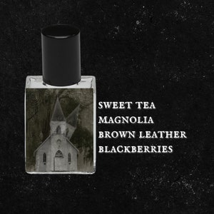 May include: A clear glass bottle with a black cap, containing a fragrance oil. The label reads "Sweet Tea Magnolia Brown Leather Blackberries".