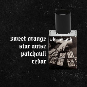 May include: A small glass bottle of perfume with a black cap. The label reads "whimsigoth" and features a vintage image of a hand holding tarot cards. The text "sweet orange, star anise, patchouli, cedar" is written below the bottle.