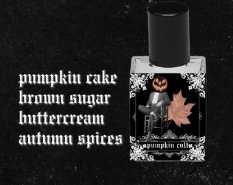 May include: A small glass bottle of perfume with a black cap. The label is black with white lettering and a graphic of a pumpkin-headed man sitting in a chair with a maple leaf. The text on the label reads "pumpkin cult". The text on the bottle reads "pumpkin cake brown sugar buttercream autumn spices".