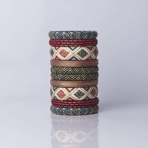 May include: A stack of colourful bangles with intricate geometric patterns. The bangles feature teal, burgundy, gold, and cream colours. The designs include diamond and zigzag patterns.