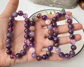 May include: A multi-coloured gemstone bracelet with purple, pink and brown beads. The bracelet is made of round beads that are strung together on a pink thread.