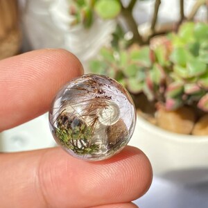 K&ouml;nnte beinhalten: Eine klare Quarzkugel mit Einschl&uuml;ssen von braunen und gr&uuml;nen haarartigen Kristallen. Die Kugel hat einen Durchmesser von etwa 1,8 cm und wiegt 10 Gramm. A- (0.7", 10g)