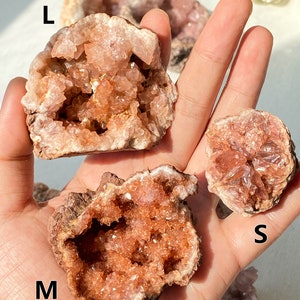 May include: Three pink amethyst geode crystals of different sizes, labelled L, M, and S. The crystals are a light pink colour with a white interior and have a rough, natural texture.