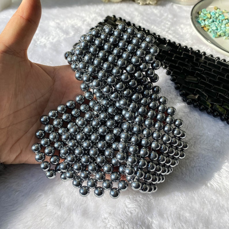 Pu&ograve; includere: Un grande ammasso di perline di metallo argentato a forma di cuore. Le perline sono disposte a griglia, creando un effetto testurizzato e tridimensionale.