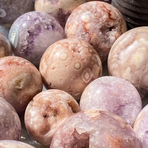 May include: A collection of pink and purple agate spheres with a variety of patterns and textures. The spheres are smooth and polished, with some showing a natural crystal formation.