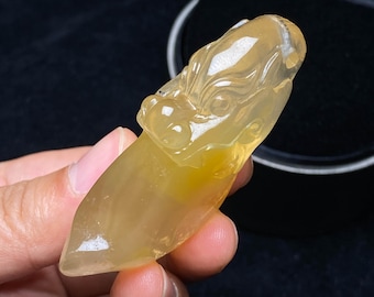May include: A translucent, yellow-toned pendant carved in the shape of a dragon's head. The dragon's features are detailed, with visible eyes and a textured surface. The pendant has a pointed, elongated body. The overall design is intricate and artistic.