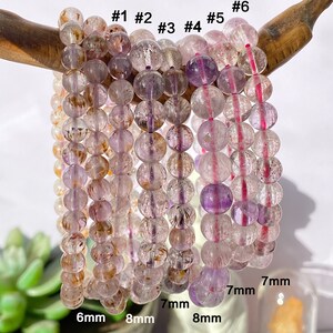 Könnte beinhalten: Sechs Amethyst-Armbänder mit unterschiedlich großen Perlen. Die Perlen haben einen Durchmesser von 6 mm bis 8 mm. Die Armbänder sind in einer Reihe angeordnet, wobei die kleinsten Perlen links und die größten rechts liegen.