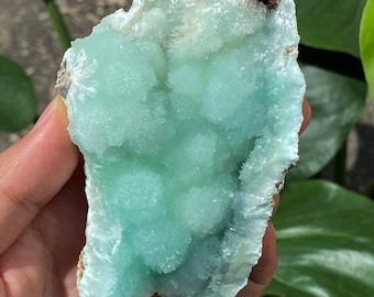 Puede incluir: Cristal de aguamarina azul verdoso claro. Superficie rugosa y texturizada con pequeñas formaciones redondeadas. El texto en la imagen dice: 107x66mm,229g. Mide aproximadamente 10,7 cm x 6,6 cm y pesa 229 g.