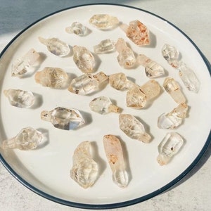 May include: A collection of clear quartz crystals with a variety of shapes and sizes, displayed on a white plate.