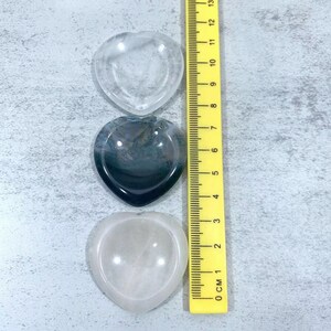 May include: Three heart-shaped crystal bowls, one clear, one black and white agate, and one pink, with a yellow ruler for size comparison.