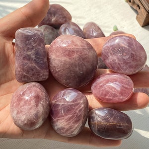 Pode incluir: Uma coleção de oito pedras de ametista roladas em vários tons de roxo e rosa. As pedras são lisas e polidas, com uma forma natural e orgânica.