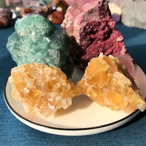 May include: Three mineral specimens on a white plate. The largest specimen is a pink and red crystal. The other two specimens are a green crystal and a yellow crystal.