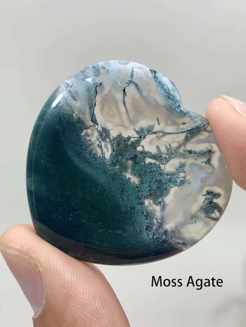 May include: A heart-shaped moss agate with green and white patterns. Moss agate is a type of chalcedony that contains inclusions of green chlorite.