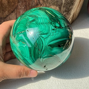 May include: A green malachite sphere with intricate swirling patterns and a polished finish. The sphere has a natural crack running through it.