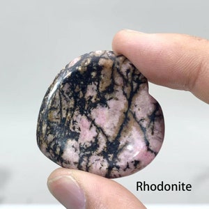 May include: A heart-shaped polished Rhodonite stone with a pink and black marbled pattern. Rhodonite is a stone that is said to promote love, compassion, and emotional healing.
