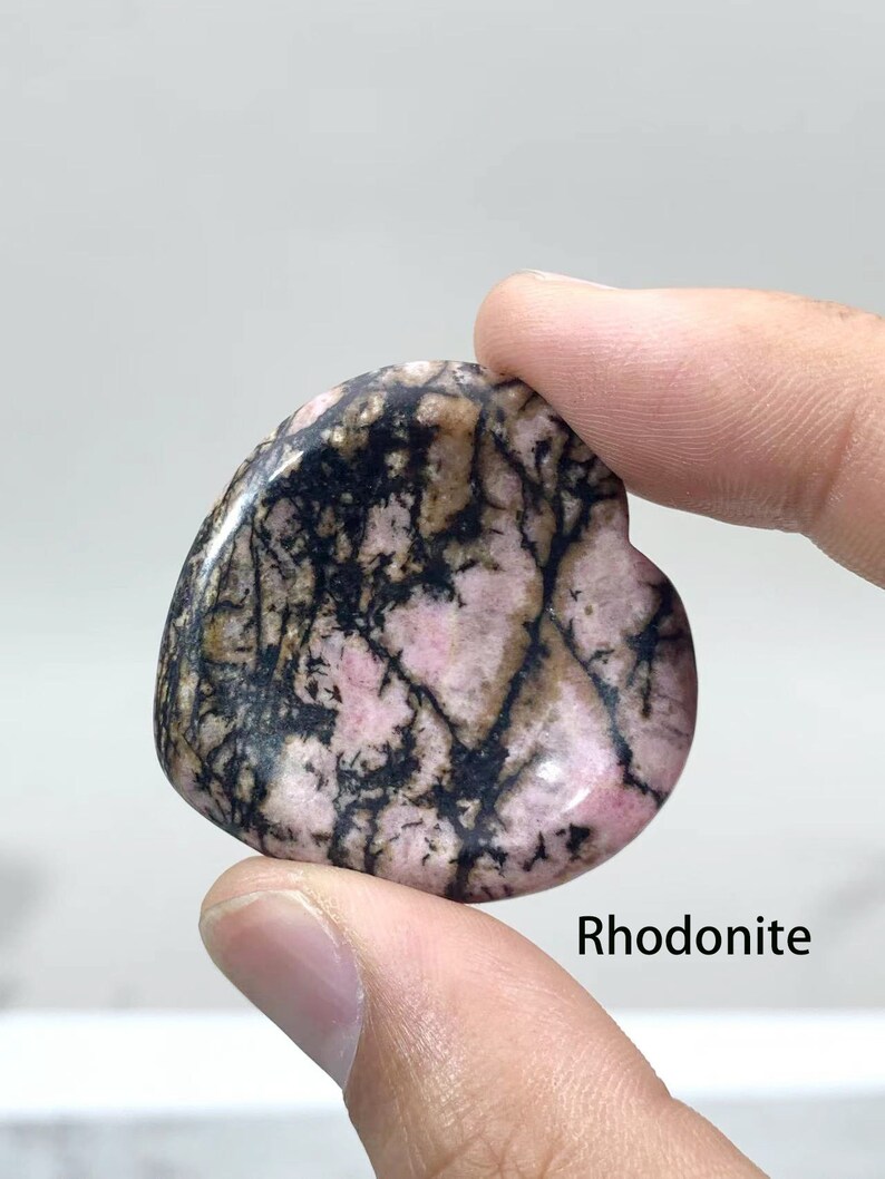 May include: A heart-shaped polished Rhodonite stone with a pink and black marbled pattern. Rhodonite is a stone that is said to promote love, compassion, and emotional healing.