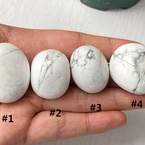 May include: Four white Howlite tumbled stones, numbered 1 through 4, are displayed on a hand. The stones are smooth and have a white and gray marbled pattern.