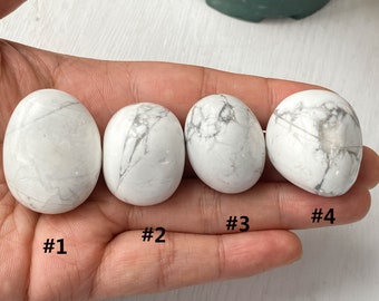 Könnte beinhalten: Vier weiße Howlith-Trommelsteine, nummeriert von 1 bis 4, werden auf einer Hand gezeigt. Die Steine sind glatt und haben ein weißes und graues Marmormuster.