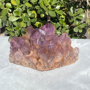 May include: A large amethyst crystal cluster with a purple and white color. The crystal is rough and has a natural, raw look.
