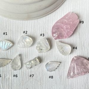May include: Ten carved gemstone pendants, including wings, flowers, and a fan shape. The pendants are made of white moonstone and pink rose quartz.