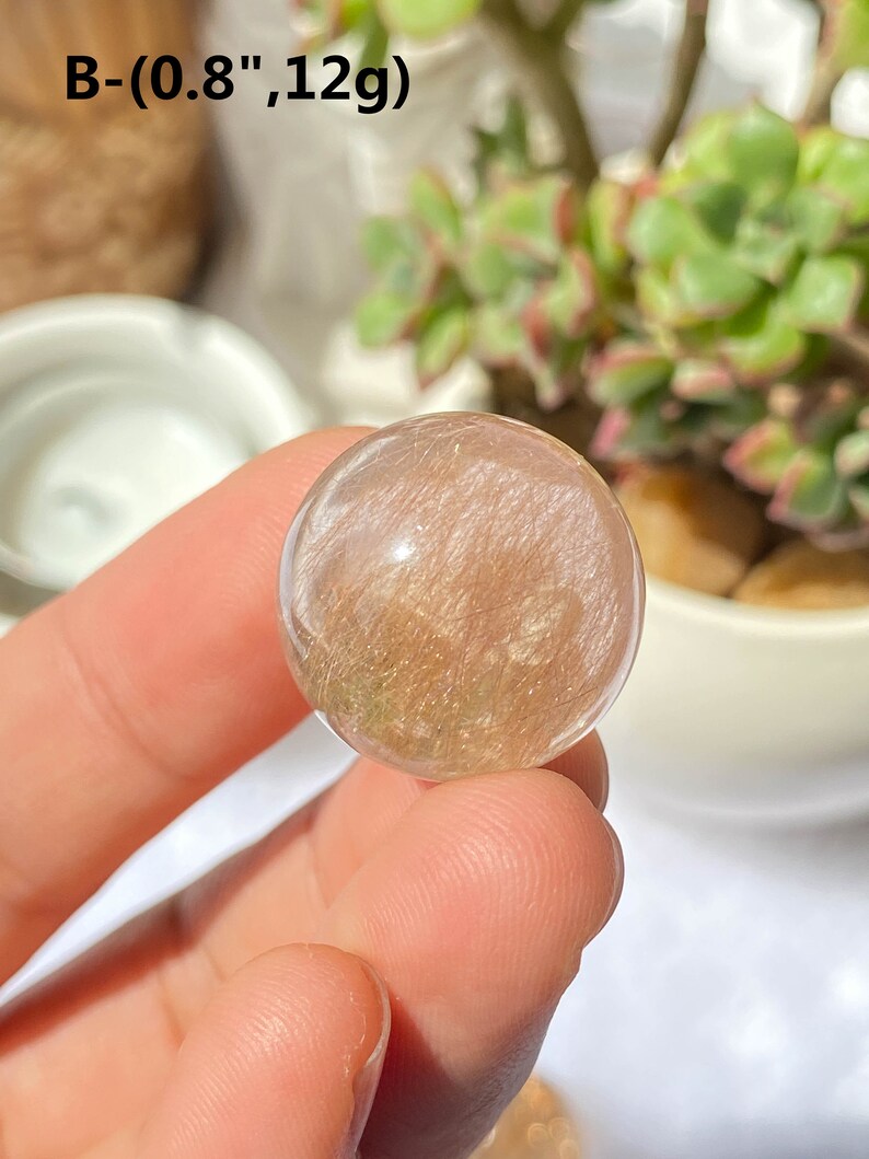 K&ouml;nnte beinhalten: Eine klare, durchscheinende Kugel mit goldenen Flocken und einem leichten Rosaton. Die Kugel hat einen Durchmesser von etwa 2 cm und wiegt 12 Gramm. B-(0.8",12g)