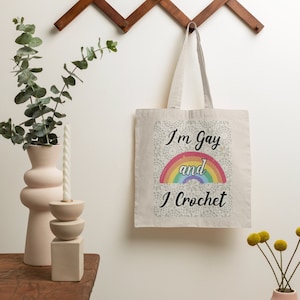 K&ouml;nnte beinhalten: Eine wei&szlig;e Einkaufstasche mit einem Regenbogen und dem Text "I'm Gay and I Crochet".