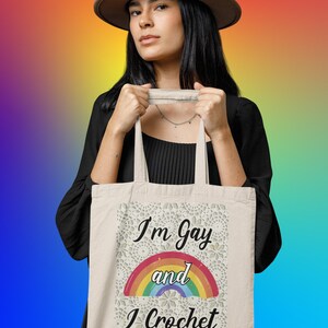 K&ouml;nnte beinhalten: Eine wei&szlig;e Einkaufstasche mit einem Regenbogen und dem Text "I'm Gay and I Crochet".
