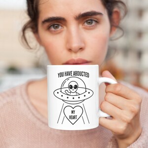 May include: White ceramic mug with a black and white illustration of an alien in a flying saucer. The text "You have abducted my heart" is printed on the mug.