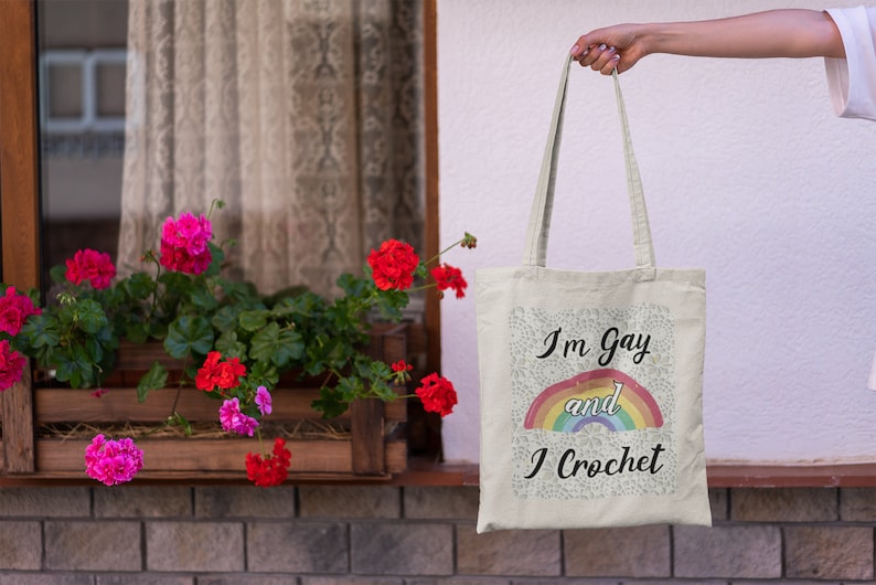 K&ouml;nnte beinhalten: Eine wei&szlig;e Einkaufstasche mit einem Regenbogen und dem Text "I'm Gay and I Crochet".