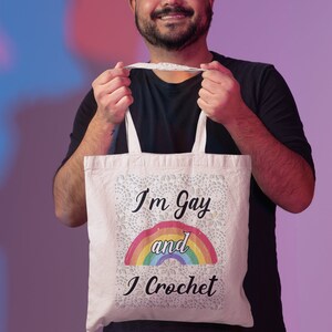 K&ouml;nnte beinhalten: Eine wei&szlig;e Einkaufstasche mit einem Regenbogen und dem Text "I'm Gay and I Crochet".