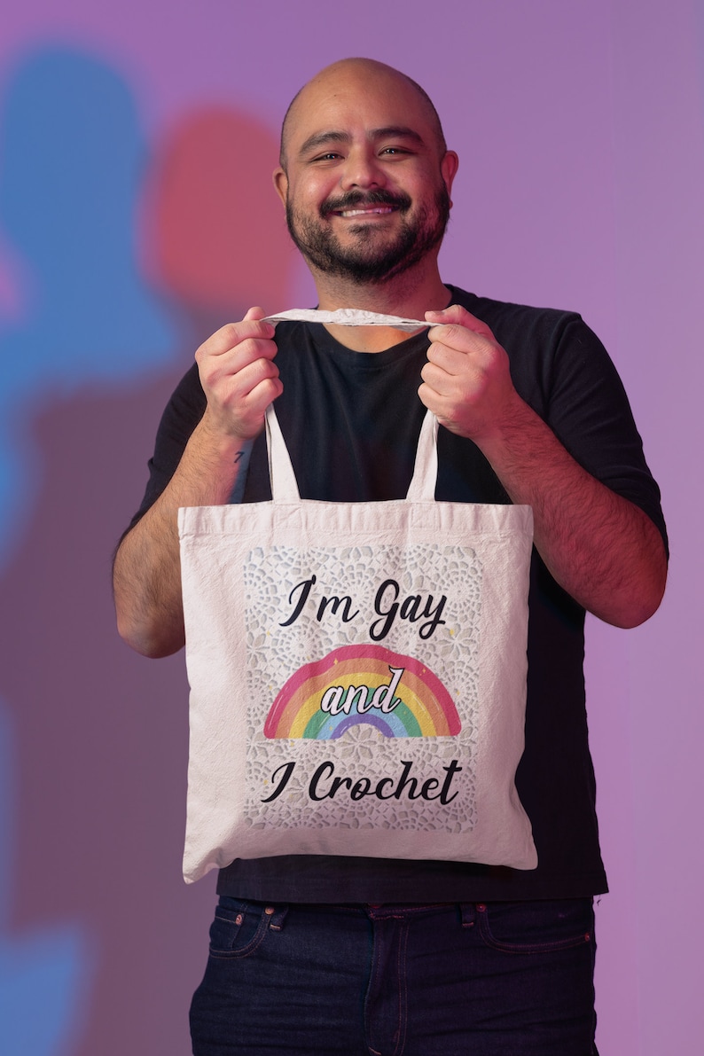 K&ouml;nnte beinhalten: Eine wei&szlig;e Einkaufstasche mit einem Regenbogen und dem Text "I'm Gay and I Crochet".