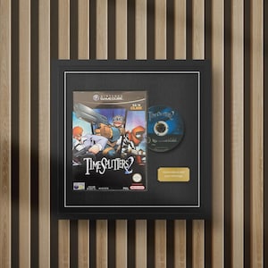 May include: A framed display featuring the TimeSplitters 2 video game case for Nintendo GameCube, the game disc, and a small gold plaque with the text Personalized with your message. The items are mounted on a black background in a black frame.