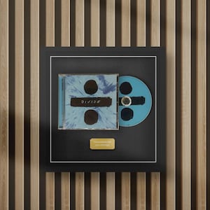 May include: A black framed display featuring the Ed Sheeran Divide CD album cover and a matching blue disc. The artwork displays a blue and white abstract pattern with the text DIVIDE. A small gold plaque at the bottom reads Personalized with your message.