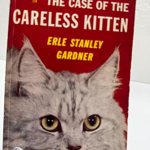 May include: Vintage paperback book cover with a red background and the title "The Case of the Careless Kitten." The cover features a close-up of a gray and white cat's face with yellow eyes. Author Erle Stanley Gardner is also listed.