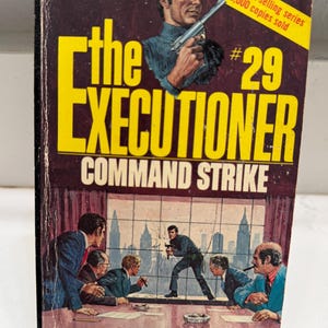 May include: Vintage paperback book cover for "The Executioner: Command Strike" by Don Pendleton. The cover features a man holding a gun, and a scene of men in suits. The title is in large yellow letters.