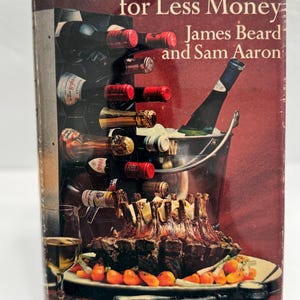May include: A vintage cookbook cover with a red background featuring a roasted meat dish with carrots and a wine bottle in a bucket of ice. The title of the book is "How to Eat Better for Less Money" by James Beard and Sam Aaron. The book cover also includes the text "With a supplement on budget wines and spirits."
