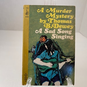 May include: A vintage paperback book cover with a green background. The title is "A Murder Mystery by Thomas B. Dewey: A Sad Song Singing". The cover features an illustration of a woman playing a guitar with a man sitting behind her.
